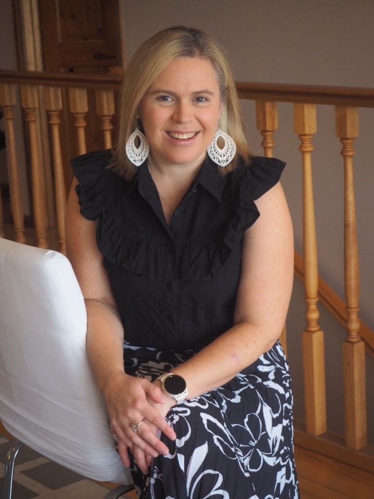 Cassie, the Director of Glorious Marketing, Sitting on a chair and smiling.
